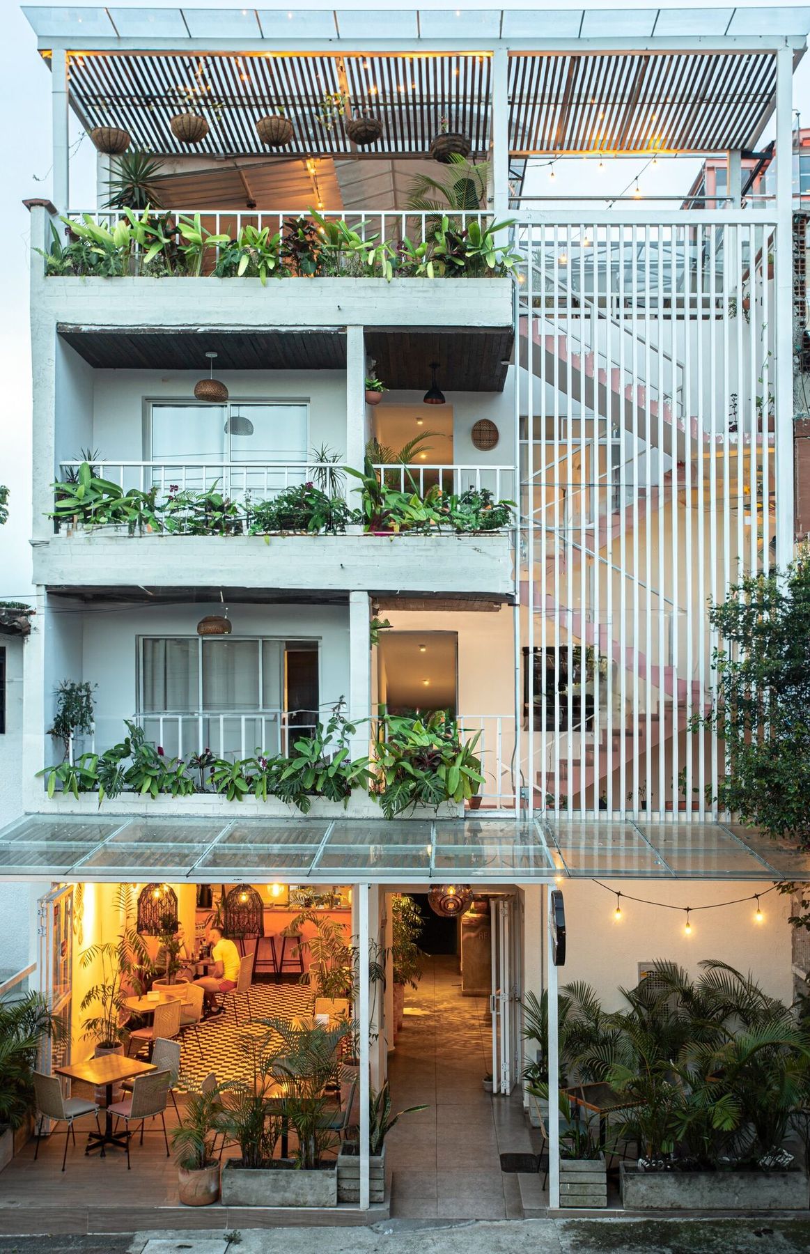 La Martina at dusk. Balconies full of plants, lights on, the café at street level lit warm.