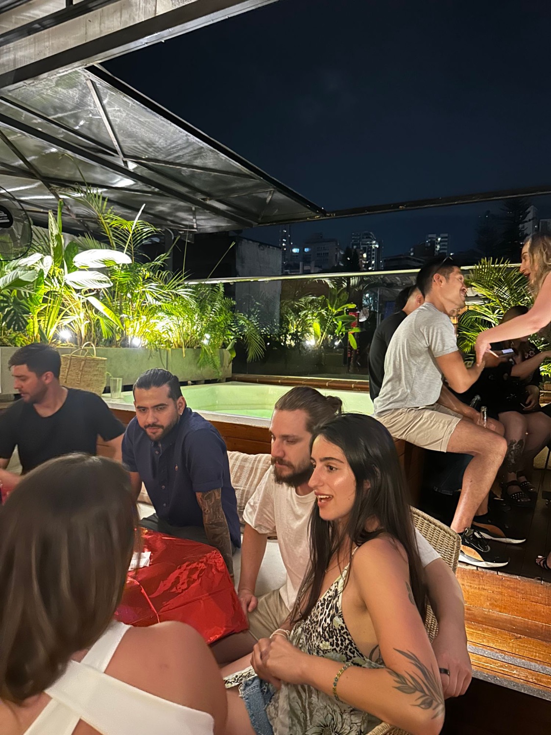 Guests talking beside the rooftop jacuzzi at night, the city behind.