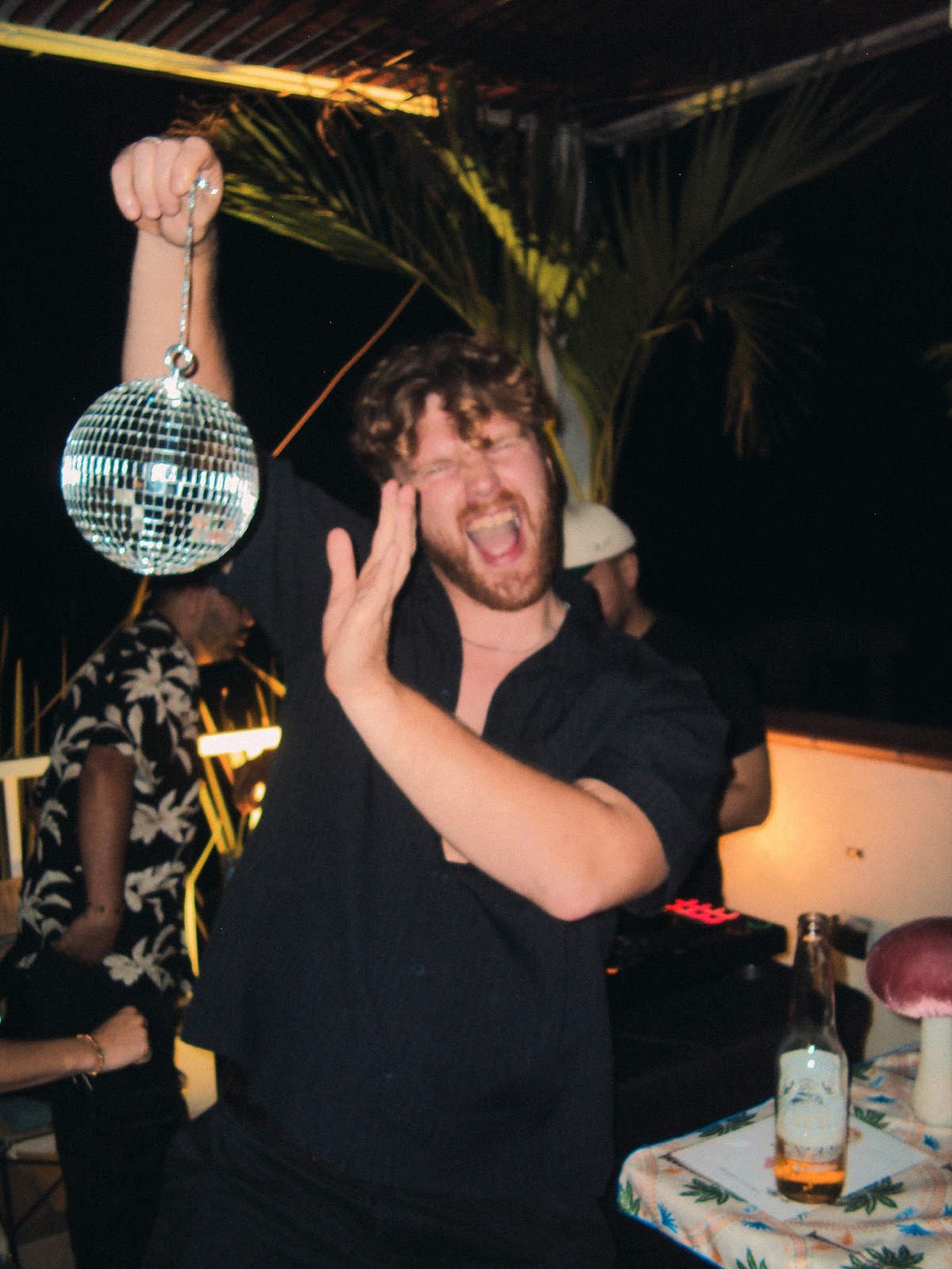 A guest dancing with a mini disco ball on the rooftop by the DJ.