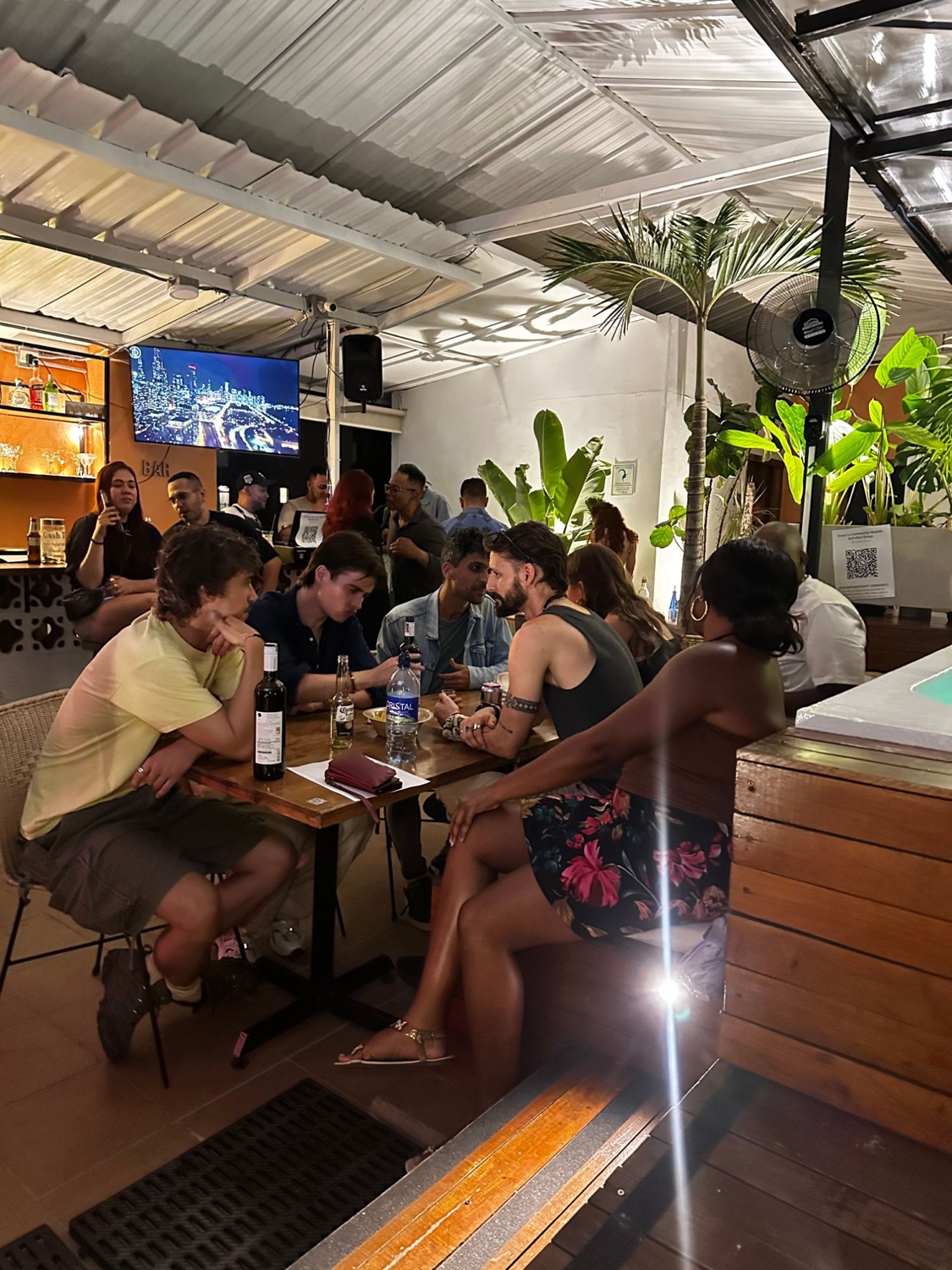 A group deep in conversation around a rooftop table, the bar busy behind them.