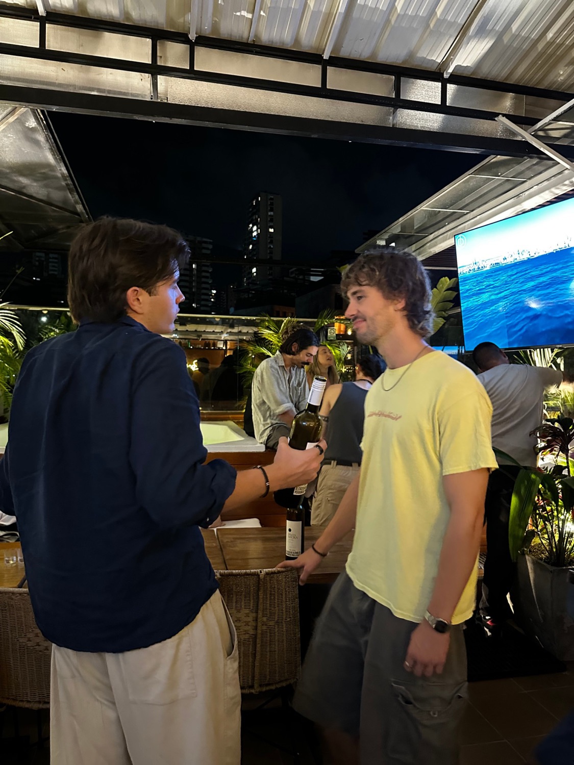 Two guests chatting on the rooftop, one holding a bottle of wine.