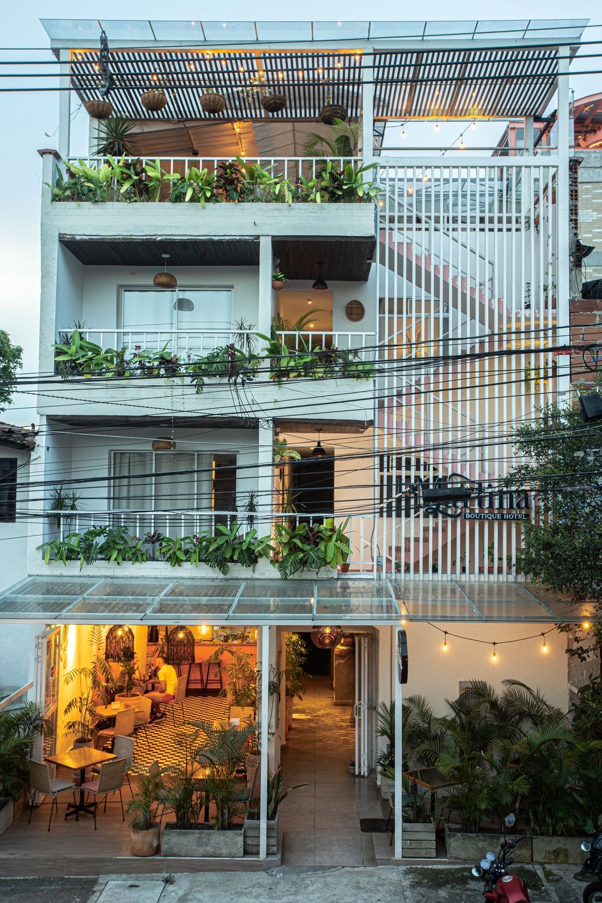 La Martina at dusk in Barrio Manila, El Poblado. Planted balconies, lights on, the café lit warm at street level.
