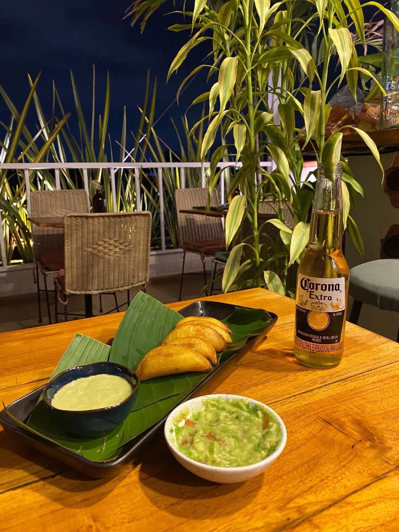 Empanadas with guacamole and a cold beer on a rooftop table at night.