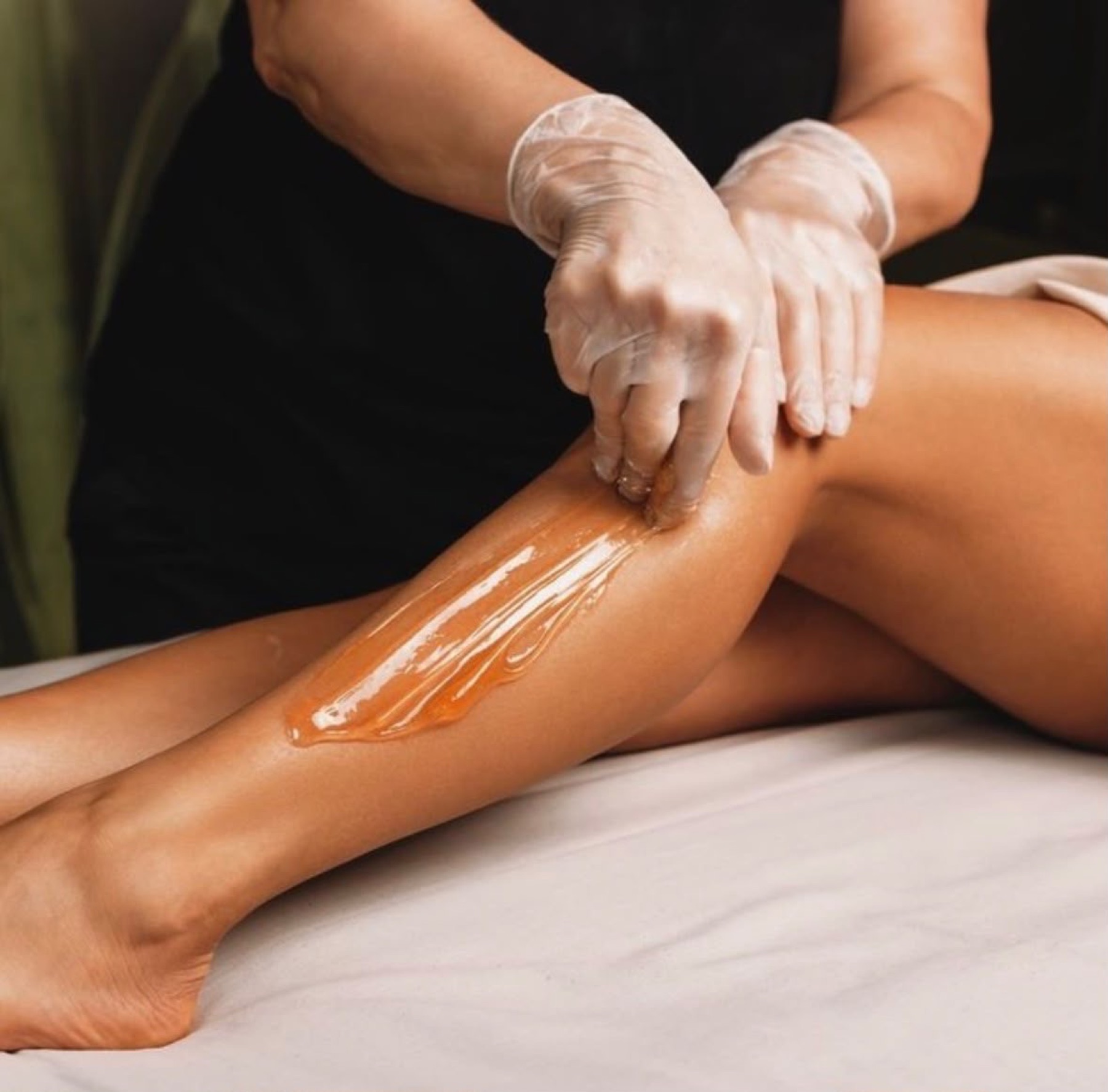 A waxing treatment on a leg, the therapist in gloves.
